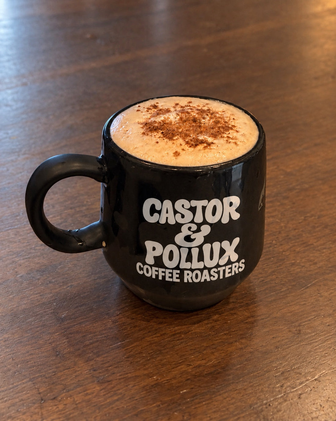 Halloween Morning coffee with foamed milk and spices in a black Castor & Pollux mug on a wood desk.