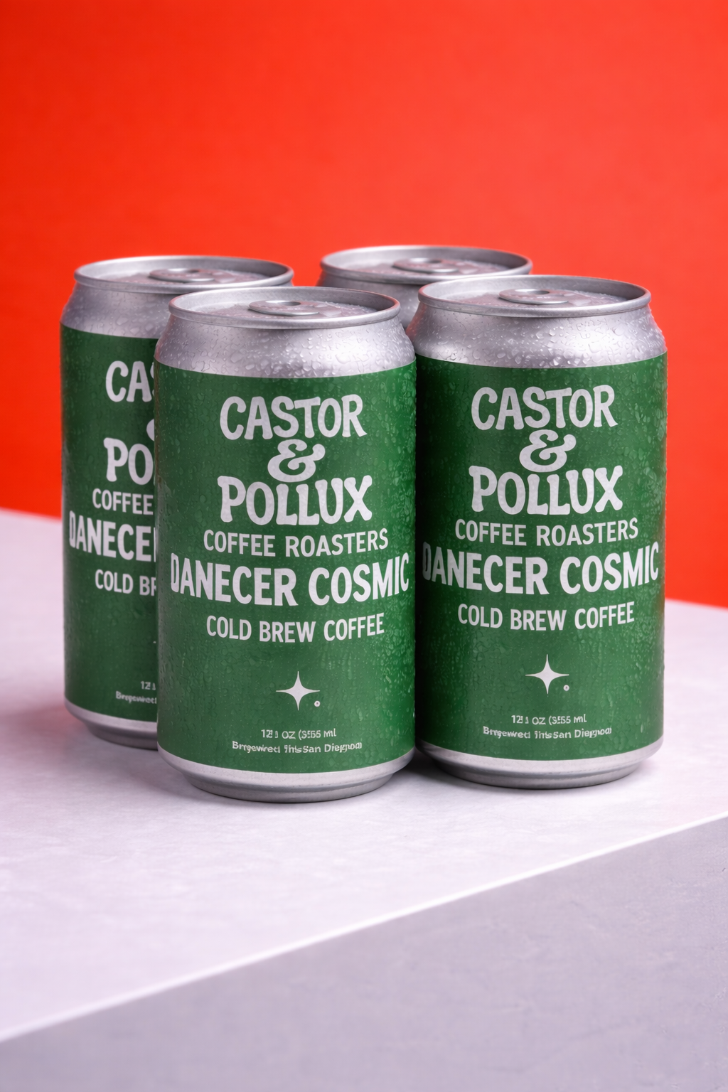 Green and silver cans of Castor & Pollux Danecer Cosmic cold brew coffee on a white and orange background.
